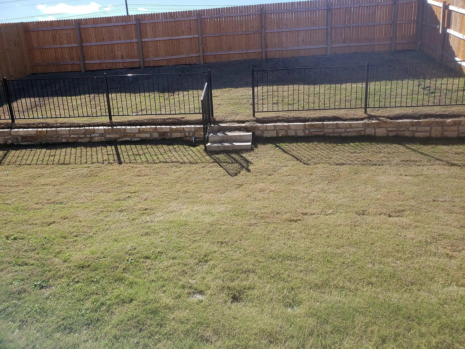 204 Brooklyn Drive Georgetown, TX 78626 - Photo 10 of 10 Tiered backyard featuring a stone retaining wall, black metal fencing, and a wooden privacy fence