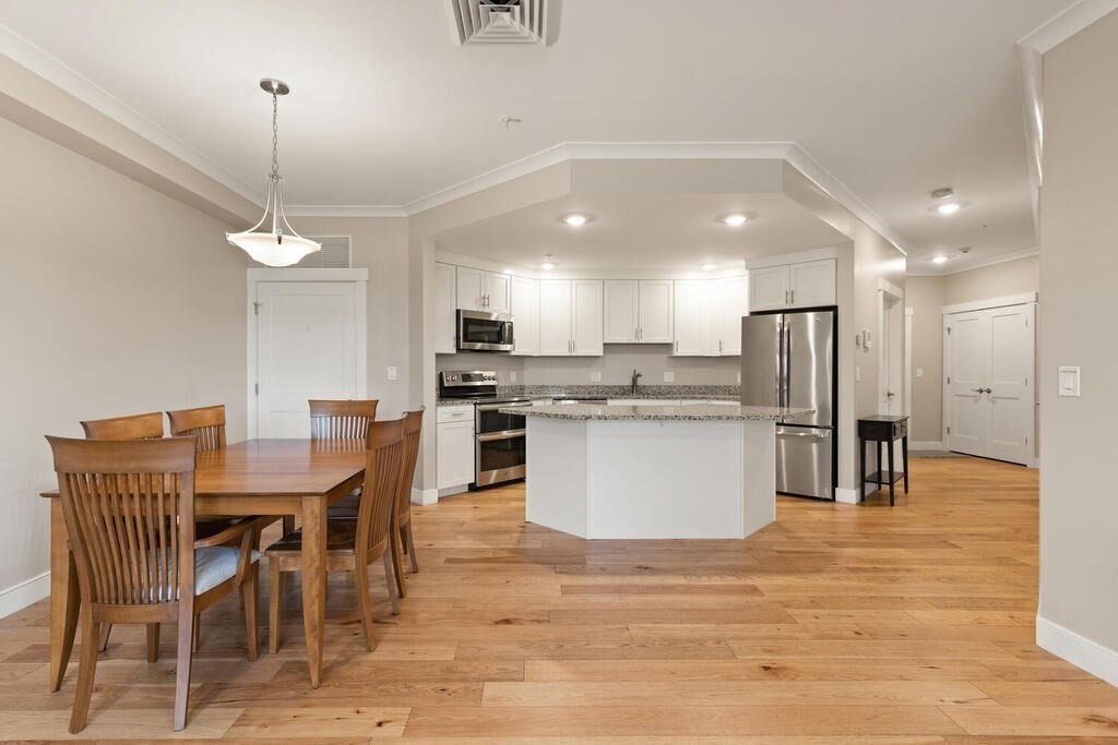 11 Executive Drive, Unit 118 Stoneham, MA 02180 - Photo 3 of 36 a kitchen with stainless steel appliances kitchen island granite countertop a stove a refrigerator a kitchen island a dining table and chairs with wooden floor