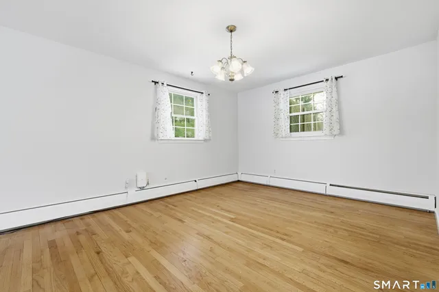 an empty room with wooden floor chandelier and windows