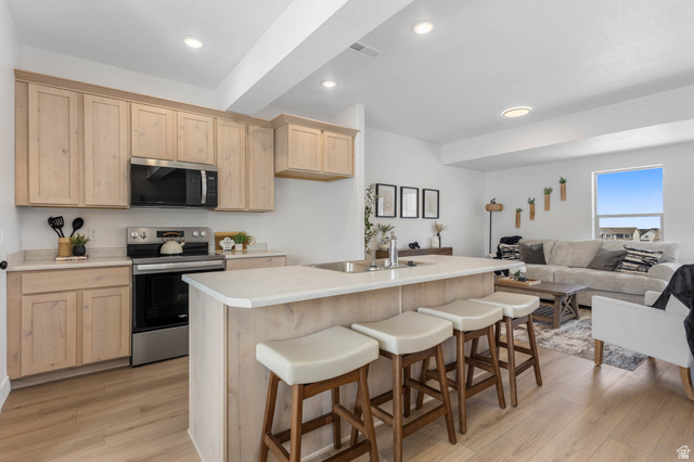 636 West Caroles Way, Unit 7 Tooele, UT 84074 - Photo 14 of 31 Open-concept kitchen featuring light wood-finish cabinetry, stainless steel appliances, and a central island with bar seating