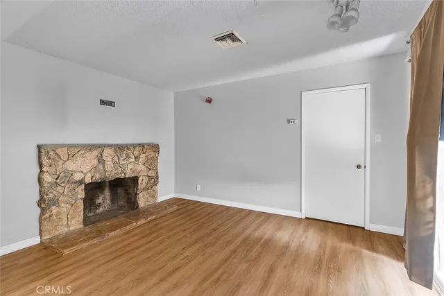 a view of an empty room with wooden floor fireplace and a window
