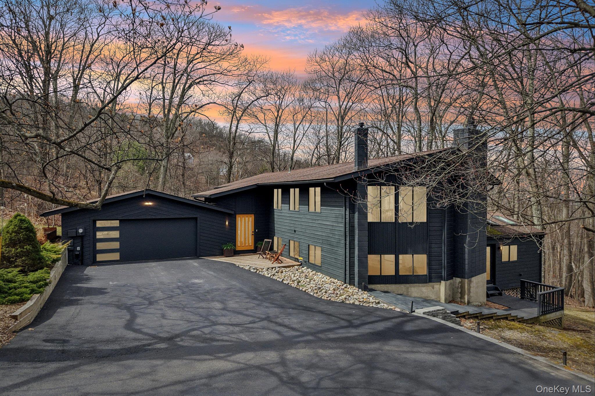 Modern home featuring a chimney, driveway, and view of wooded area