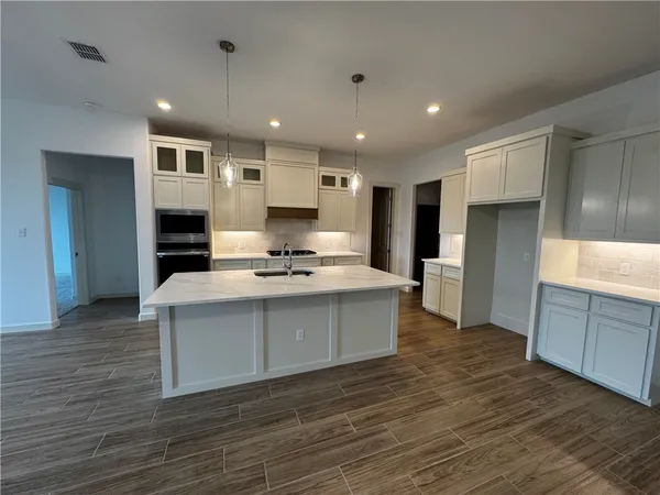 a large white kitchen with kitchen island a sink dishwasher a refrigerator and white cabinets with wooden floor