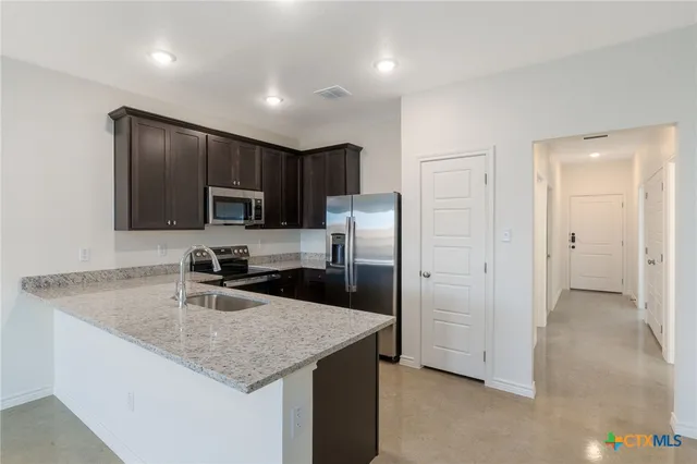 a kitchen with kitchen island granite countertop stainless steel appliances a sink stove refrigerator and cabinets