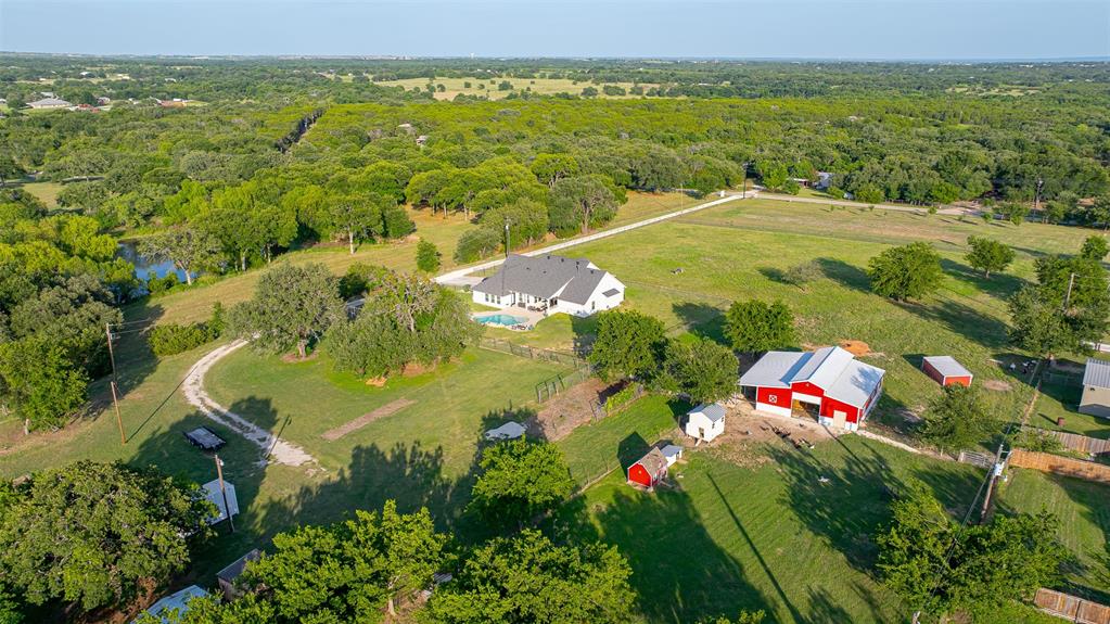 1920 Meander Road Granbury, TX 76049 - Photo 33 of 40 Expansive property featuring a white residence with a dark roof, a swimming pool, a red barn with a metal roof, and a pond surrounded by mature trees