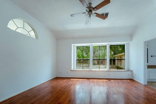 an empty room with wooden floor fan and windows