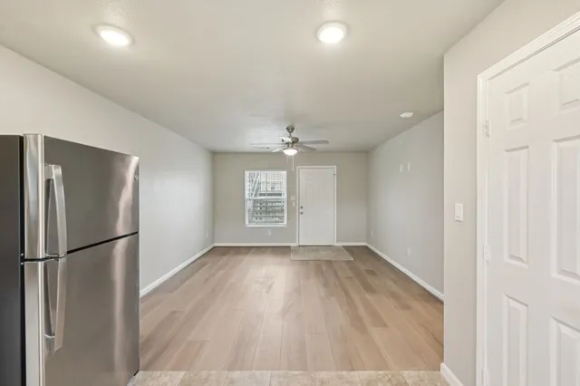 an empty room with wooden floor a ceiling fan and kitchen view