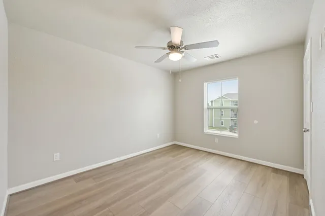 an empty room with wooden floor fan and windows