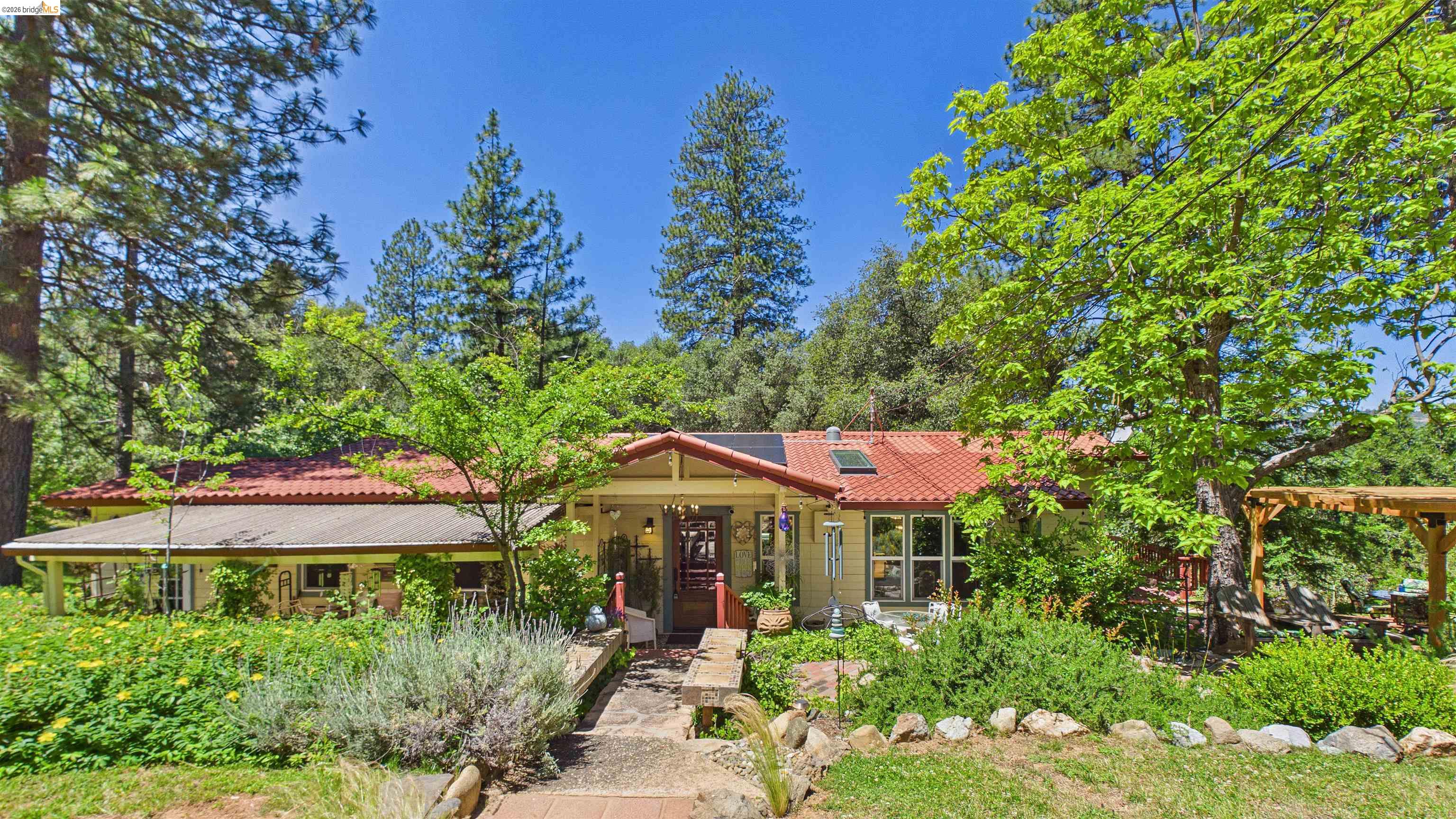 Ranch-style exterior with a red tile roof, surrounded by mature trees and lush landscaping