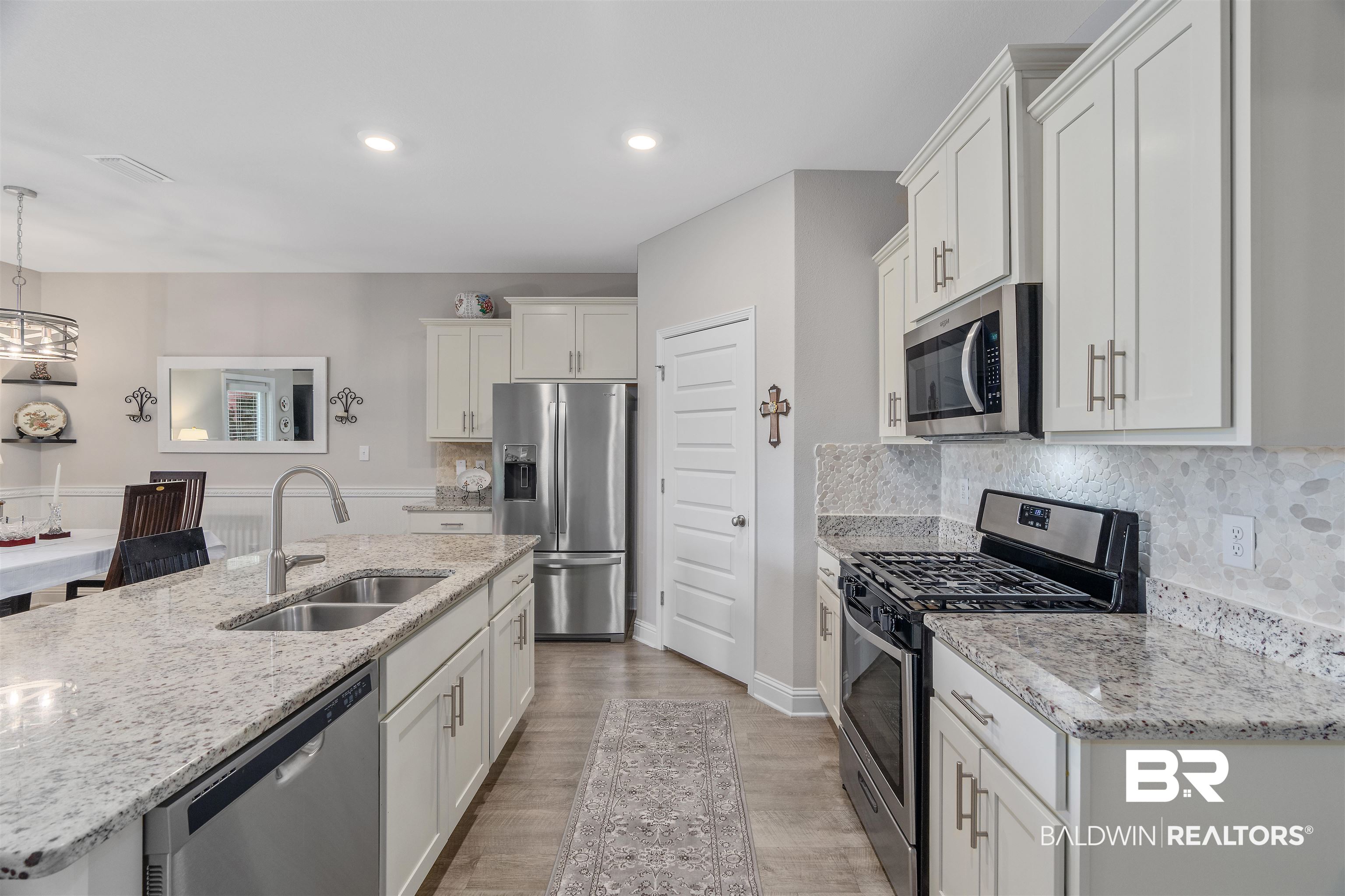 24593 Slater Mill Road Daphne, AL 36526 - Photo 12 of 32 Kitchen with stainless steel appliances, white cabinets, light wood-style floors, a kitchen island with sink, and tasteful backsplash