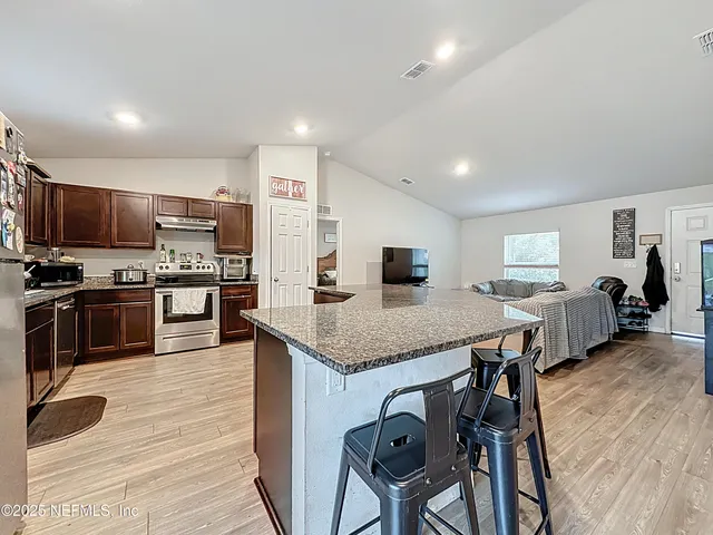 a kitchen with stainless steel appliances granite countertop a stove top oven a sink a dining table and chairs with wooden floor