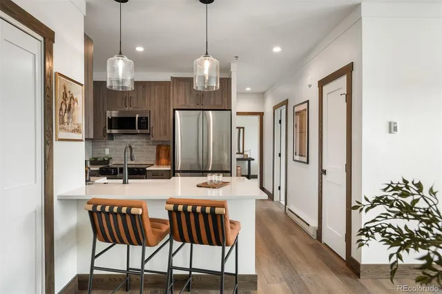 a kitchen with stainless steel appliances granite countertop a refrigerator a oven a sink a dining table and chairs with wooden floor