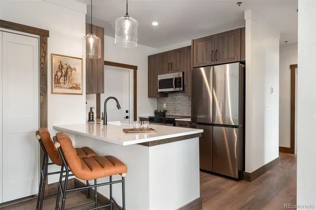 a kitchen with stainless steel appliances granite countertop a refrigerator a stove a sink cabinets a dining table and chairs