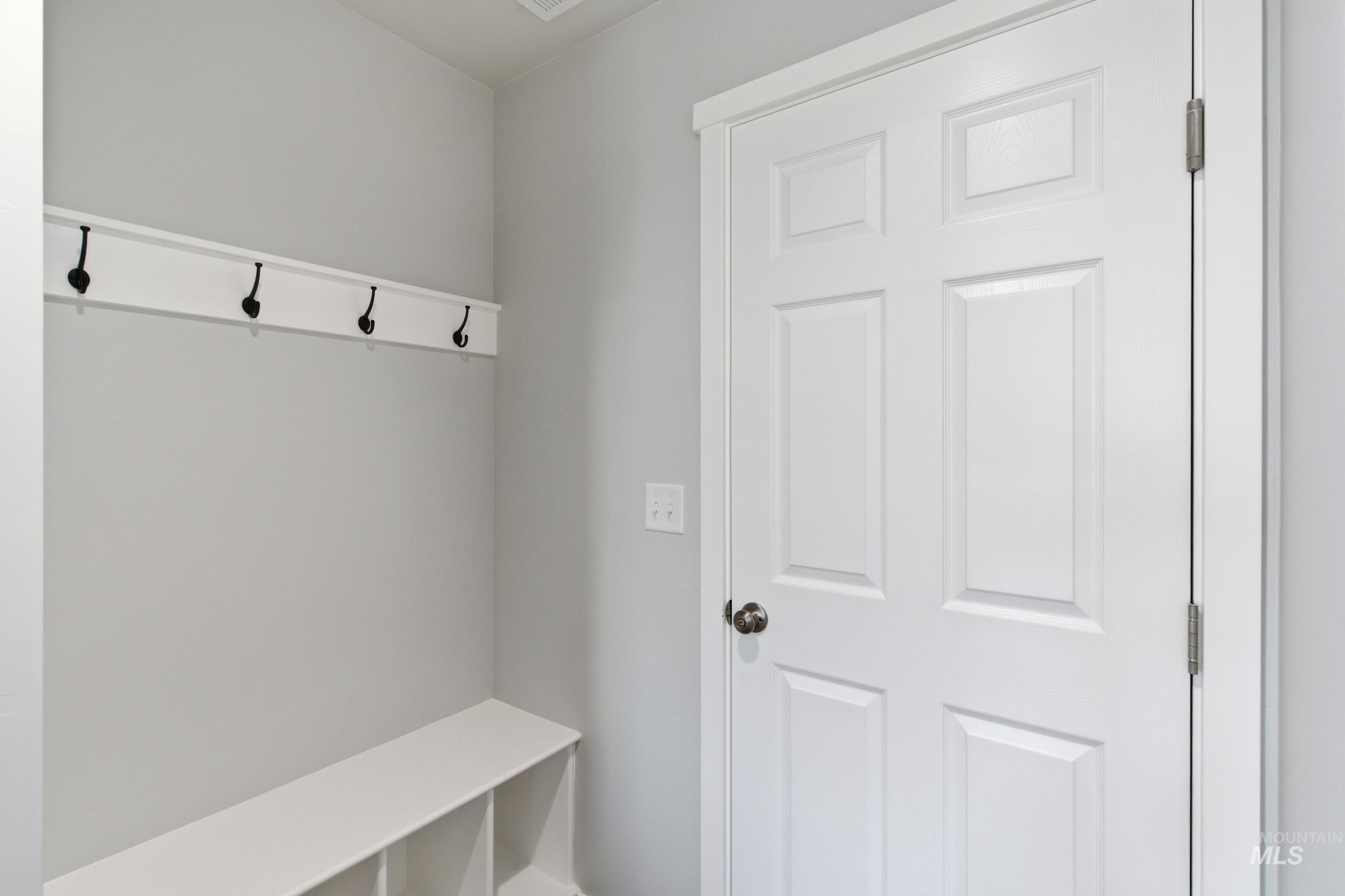 16558 Dunning Way Caldwell, ID 83607 - Photo 16 of 35 Entryway featuring a built-in bench with cubby storage, a wall-mounted coat rack with four black hooks, a white six-panel door with a black doorknob, and light gray walls