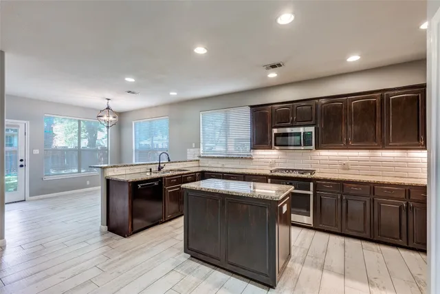 a kitchen with stainless steel appliances granite countertop wooden cabinets a sink dishwasher and a stove top oven with wooden floor