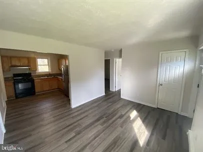 an empty room with wooden floor kitchen view and a window