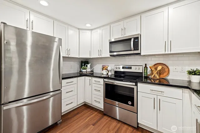 a white kitchen with stainless steel appliances granite countertop a refrigerator and a stove top oven
