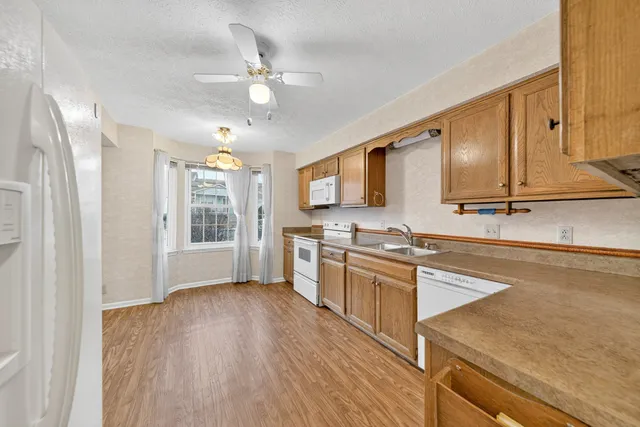 a view of an empty room with wooden floor staircase and a kitchen space