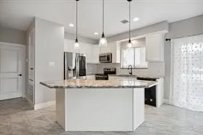 a kitchen with kitchen island granite countertop a sink a counter space appliances and cabinets