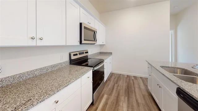 a kitchen with granite countertop a sink a stove top oven and cabinetry
