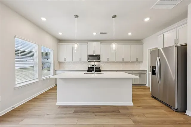 a kitchen with stainless steel appliances granite countertop a refrigerator a sink dishwasher a stove and white countertops with wooden floor