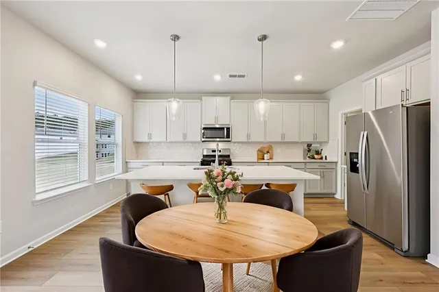 a kitchen with stainless steel appliances granite countertop a refrigerator a stove a sink a dining table and chairs