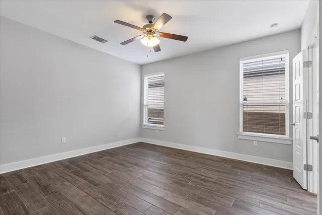 a view of an empty room with wooden floor and a ceiling fan