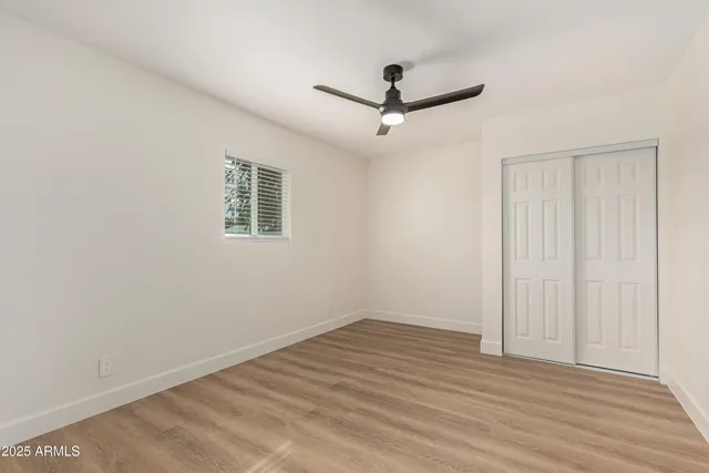 an empty room with wooden floor ceiling fan and windows
