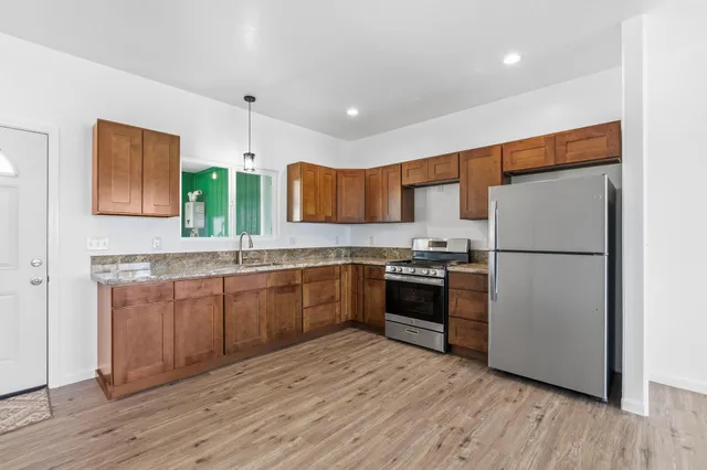 a kitchen with stainless steel appliances granite countertop a refrigerator a sink dishwasher a stove with wooden cabinets and wooden floor