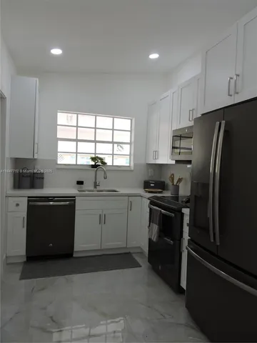 a kitchen with granite countertop white cabinets appliances a window and a sink