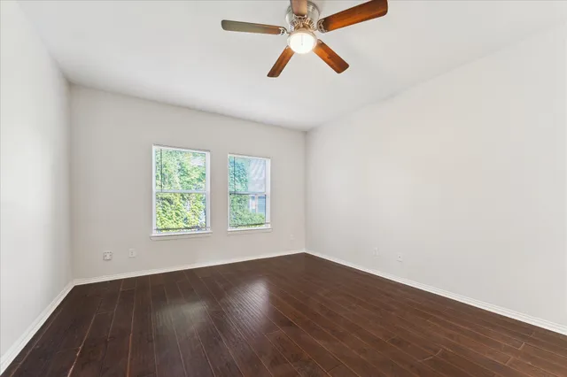 an empty room with wooden floor ceiling fan and windows
