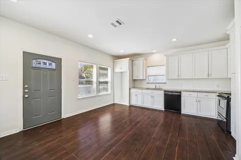 a open kitchen with granite countertop white cabinets a sink dishwasher and a stove with wooden floor