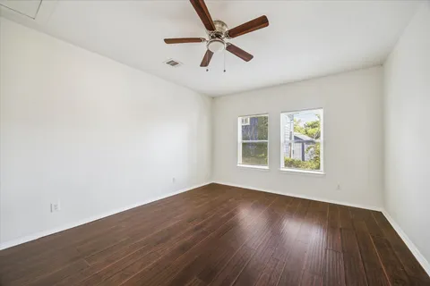 an empty room with wooden floor ceiling fan and windows