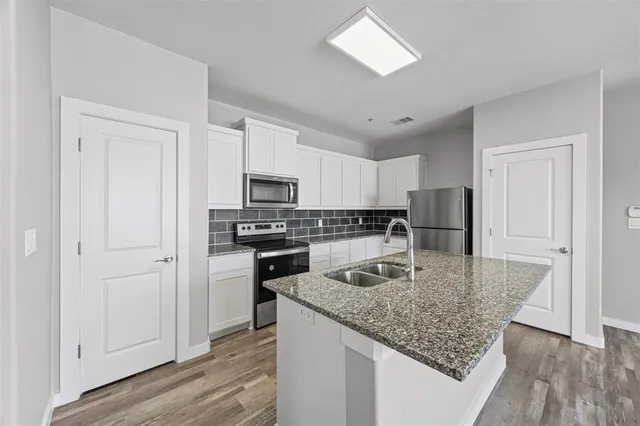 a kitchen with stainless steel appliances granite countertop a stove top oven a refrigerator a sink and white cabinets