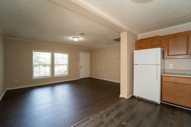 an empty room with wooden floor and a refrigerator