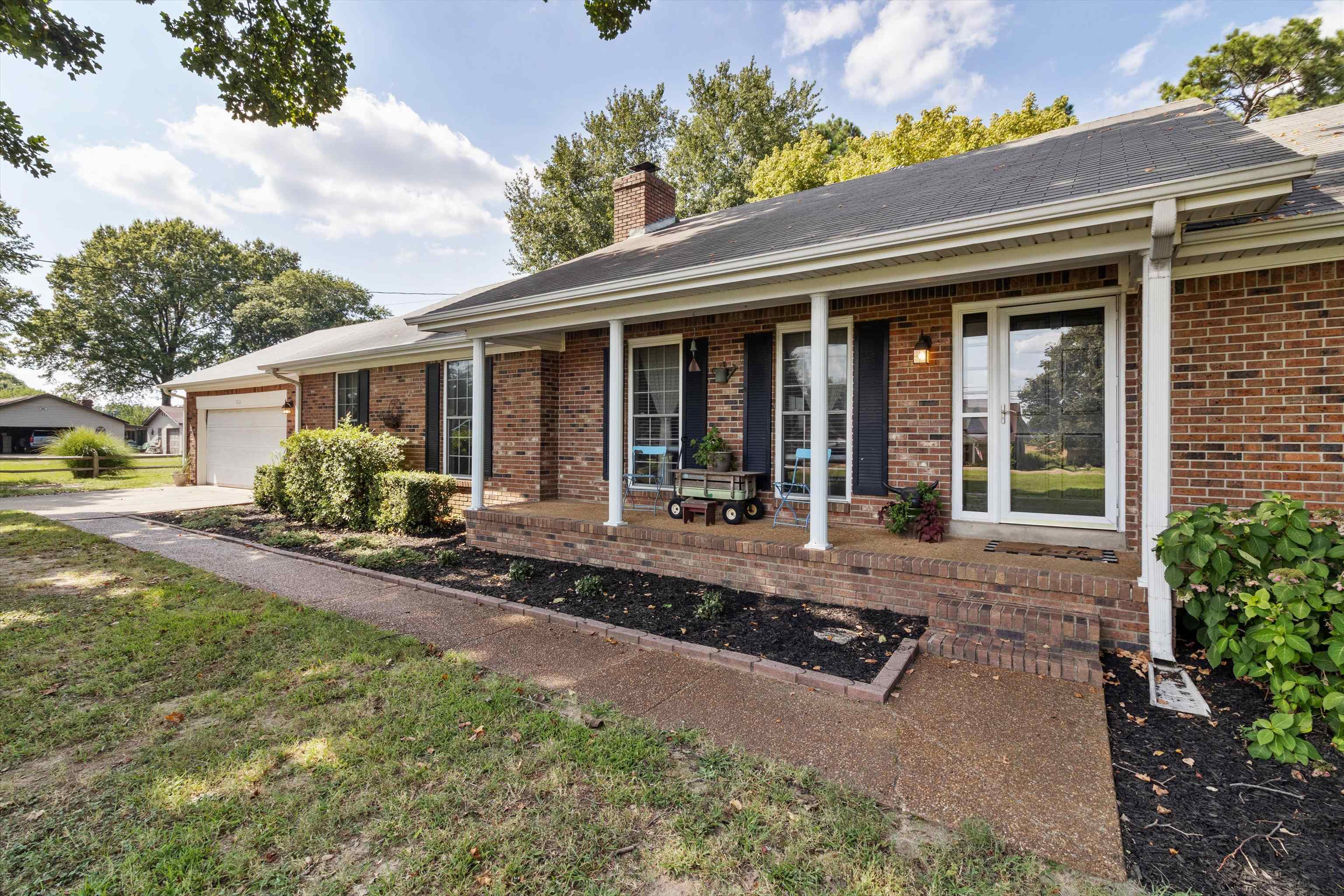 202 Holly Grove Road Covington, TN 38019 - Photo 2 of 32 View of front of home featuring covered porch, brick siding, a chimney, an attached garage, and concrete driveway