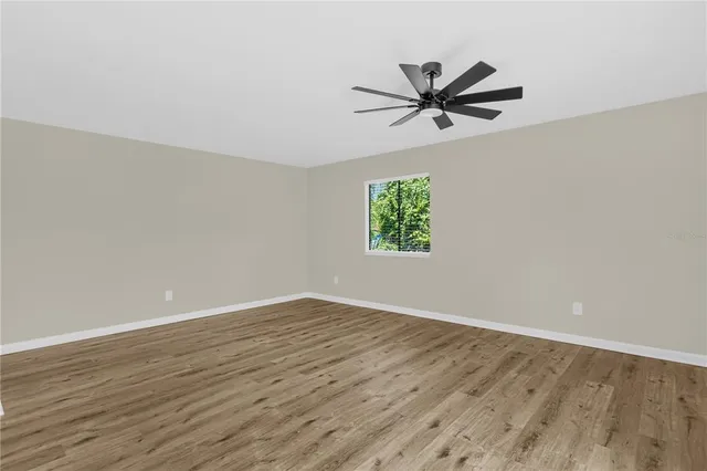 an empty room with wooden floor a ceiling fan and windows