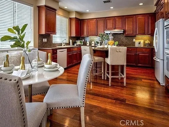 a kitchen with stainless steel appliances kitchen island granite countertop a table chairs and a refrigerator