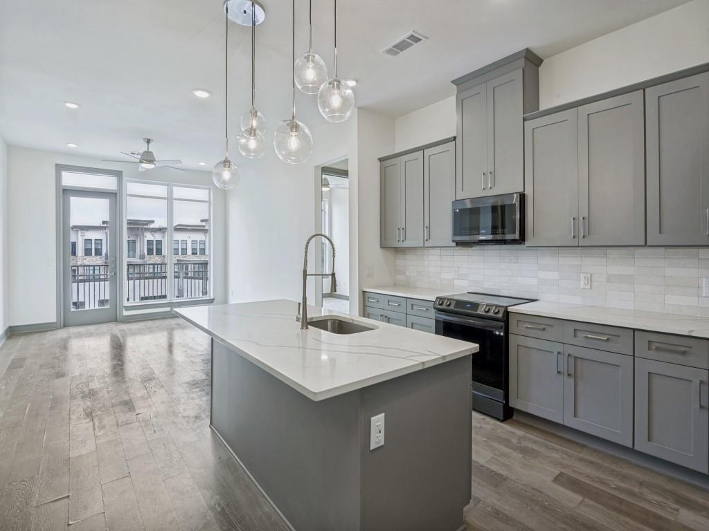 a kitchen with stainless steel appliances granite countertop a sink a stove a refrigerator and island with wooden floor