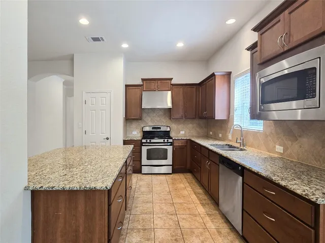 a kitchen with stainless steel appliances granite countertop wooden cabinets a stove top oven a sink and dishwasher