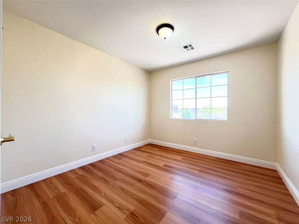 9891 Ridge Hill Avenue Las Vegas, NV 89147 - Photo 22 of 29 Rich hardwood-style flooring extends across this naturally illuminated bedroom, offering a warm and inviting atmosphere.
