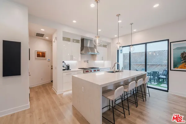 a open kitchen with stainless steel appliances granite countertop a stove a refrigerator a oven a sink a dining table and chairs with wooden floor