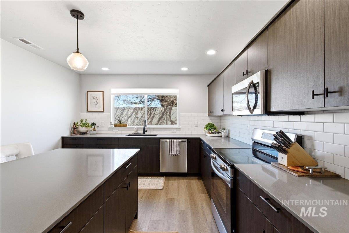 5392 South Memory Way Meridian, ID 83642 - Photo 13 of 39 Kitchen featuring stainless steel appliances, light wood finished floors, dark wood finish cabinetry, pendant lighting, and decorative backsplash