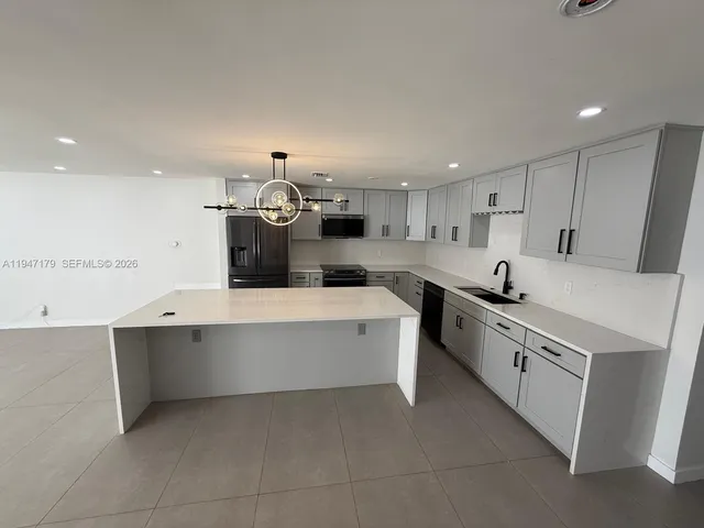 a large kitchen with a large counter top a sink stainless steel appliances and cabinets