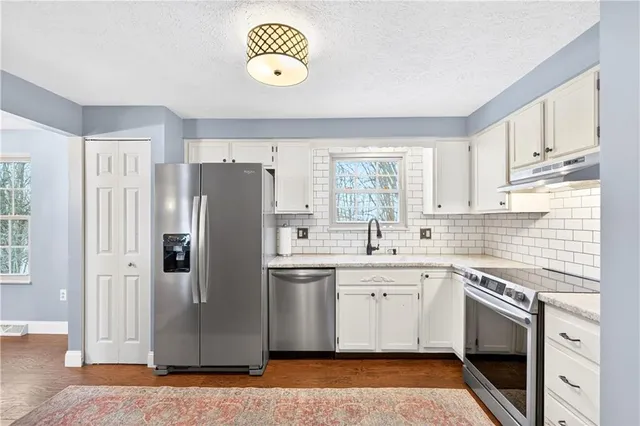 a kitchen with stainless steel appliances granite countertop a refrigerator a sink a stove and white cabinets with wooden floor