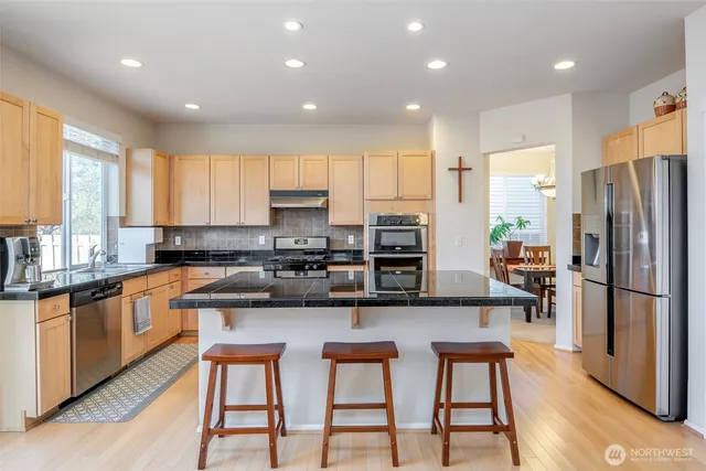 a kitchen with stainless steel appliances granite countertop a stove a sink a refrigerator white cabinets and wooden floor