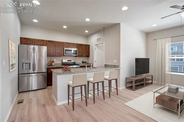 a kitchen with stainless steel appliances a refrigerator a stove top oven a sink dishwasher a dining table and chairs with wooden floor