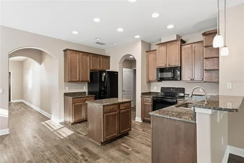 a kitchen with kitchen island granite countertop a stove top oven a sink dishwasher a refrigerator and cabinets with wooden floor