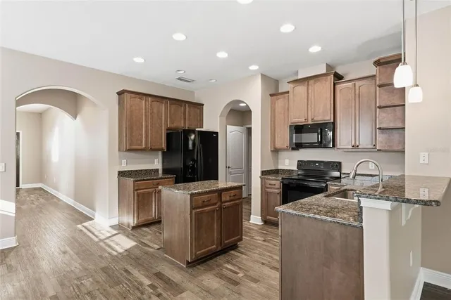 a kitchen with kitchen island granite countertop a stove top oven a sink dishwasher a refrigerator and cabinets with wooden floor