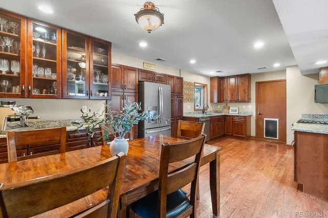 a kitchen with stainless steel appliances kitchen island granite countertop a stove a refrigerator a sink a dining table and chairs with wooden floor